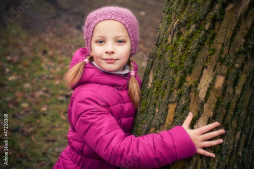 Little girl near tree in autumn or winter park.