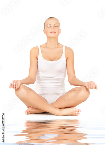 woman practicing yoga lotus pose on white sand