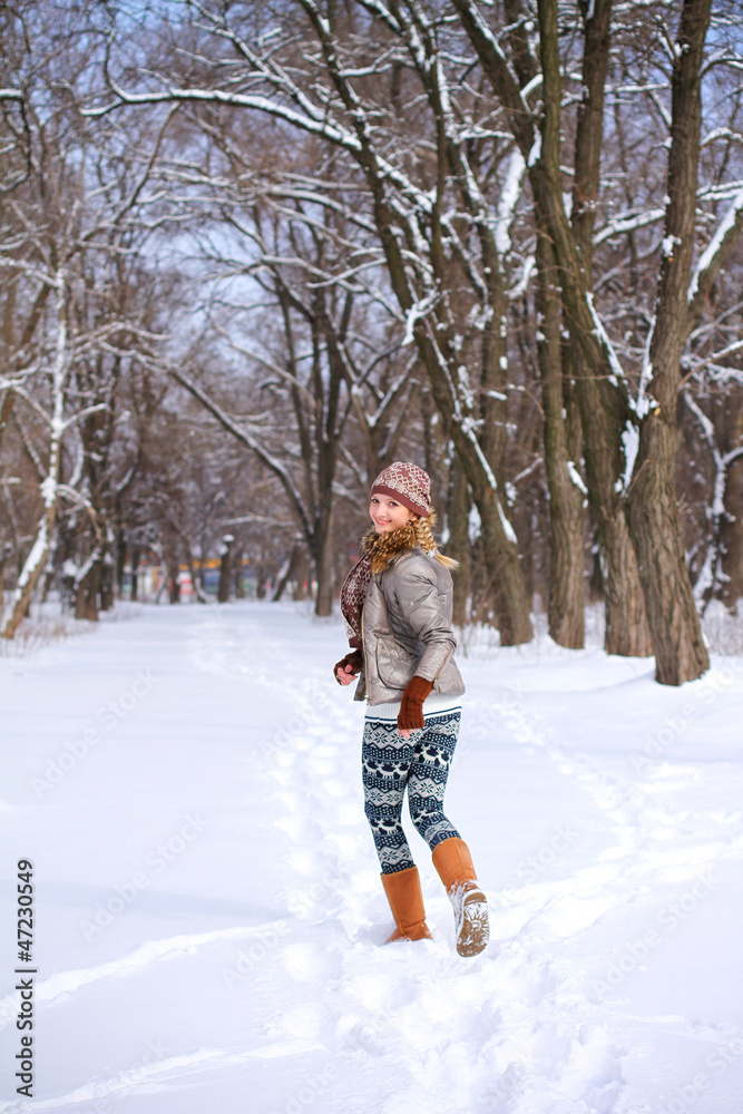 Smiling girl running through the snow in a winter park outdoors