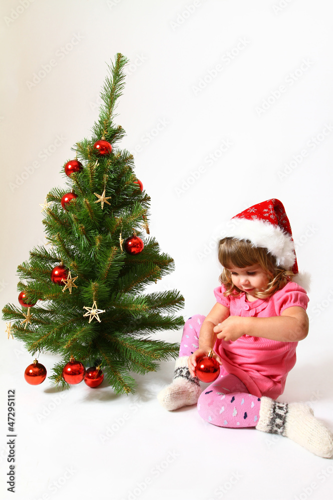 Sweet baby in a hat of Santa Claus sitting near New Year or Chri
