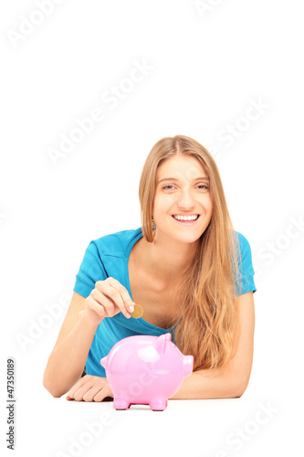 Smiling female putting a coin into a piggy bank