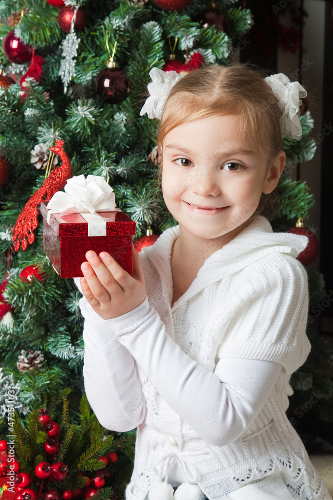 Happy girl in white jacket with gift near christmas tree