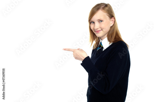 Pretty schoolgirl pointing towards copy space area
