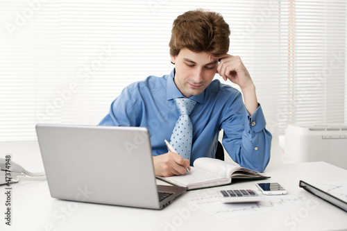 manager sitting at desk in the office, working on laptop