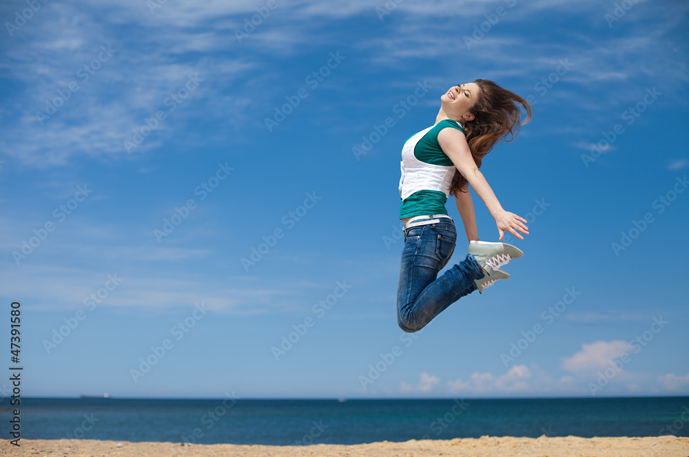 sporty woman jumping against the clear blue sky on beach