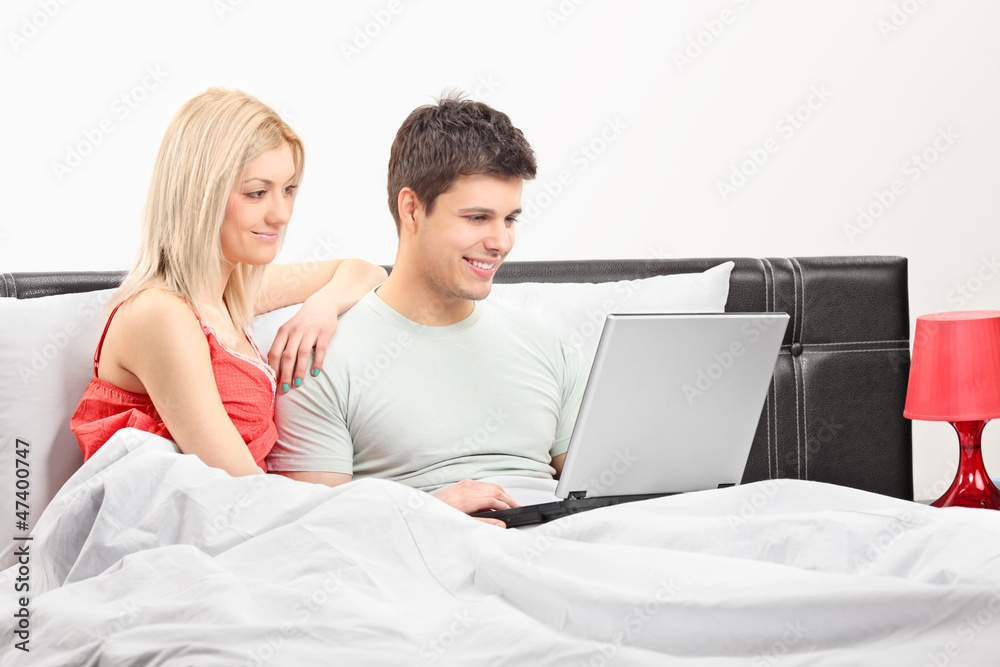 Young couple lying on a bed and working on a laptop