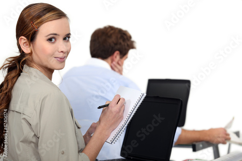 female employee writing notes near a colleague © auremar