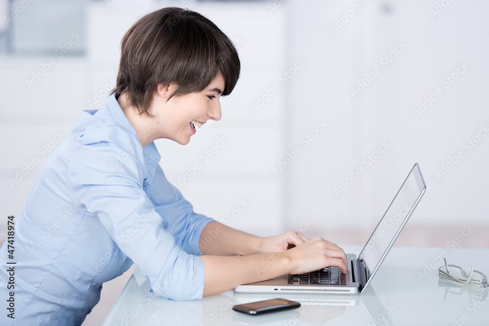 lächelnde frau im büro schaut auf ihren laptop lächelnde frau im büro schaut auf ihren laptop