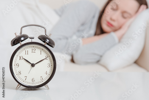 Alarm clock on table and woman sleeping