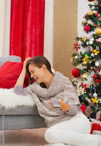 Laughing young woman watching TV near Christmas tree © Alliance