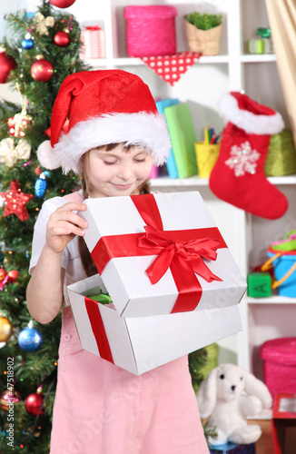 A little girl opens a gift in festively decorated room © Africa Studio