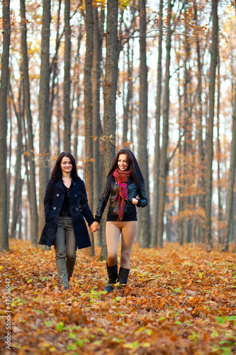 Two happy girlfriends walking in the woods while holding hands