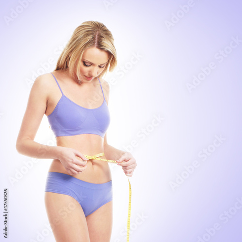 A blond woman on a blue swimsuit measuring her waist © Acronym