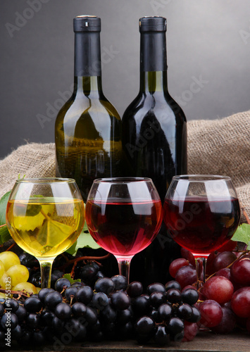 bottles and glasses of wine and grapes on grey background