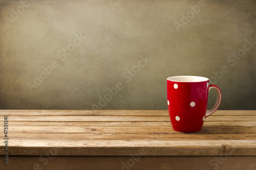 Red cup with dots on wooden table over grunge background