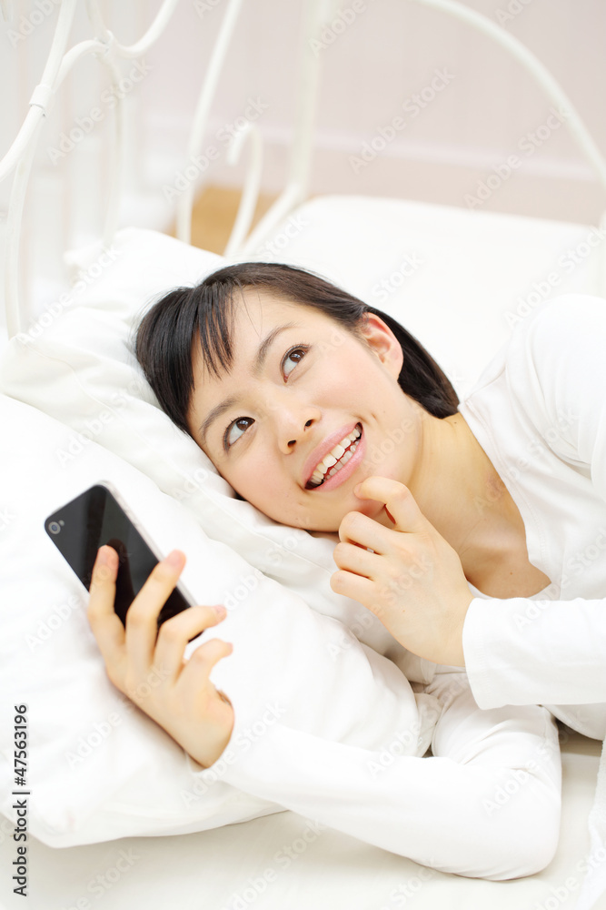 スマートフォンを寝ながら使う女の子 スマートフォンを寝ながら使う女の子