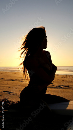 A girl sits in silhouette during the morning sunrise on the beac