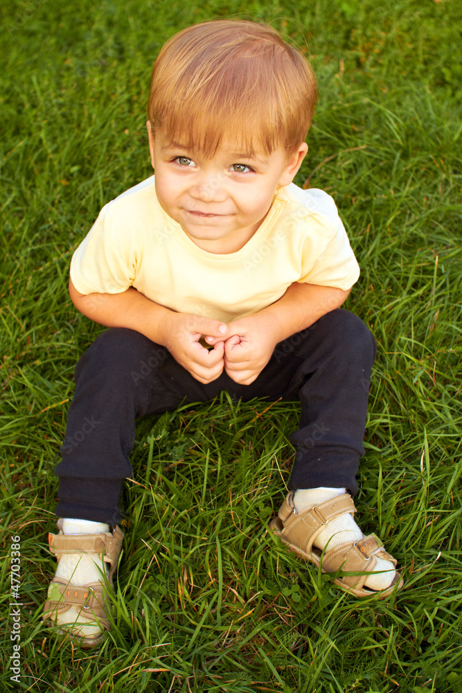 Smiling little boy sitting in fresh grass Smiling little boy sitting in fresh grass