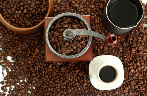 Coffee grinder, turk and cup of coffee on beans background