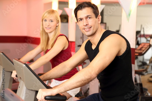 Attractive woman and a man cycling in a gym