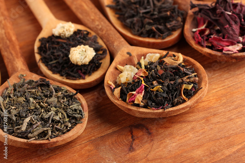 assortment of dry tea in spoons, on wooden background