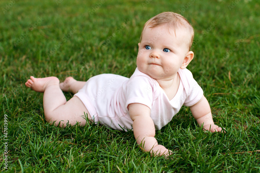 Cute baby lying on her tummy enjoying texture of soft grass Cute baby lying on her tummy enjoying texture of soft grass