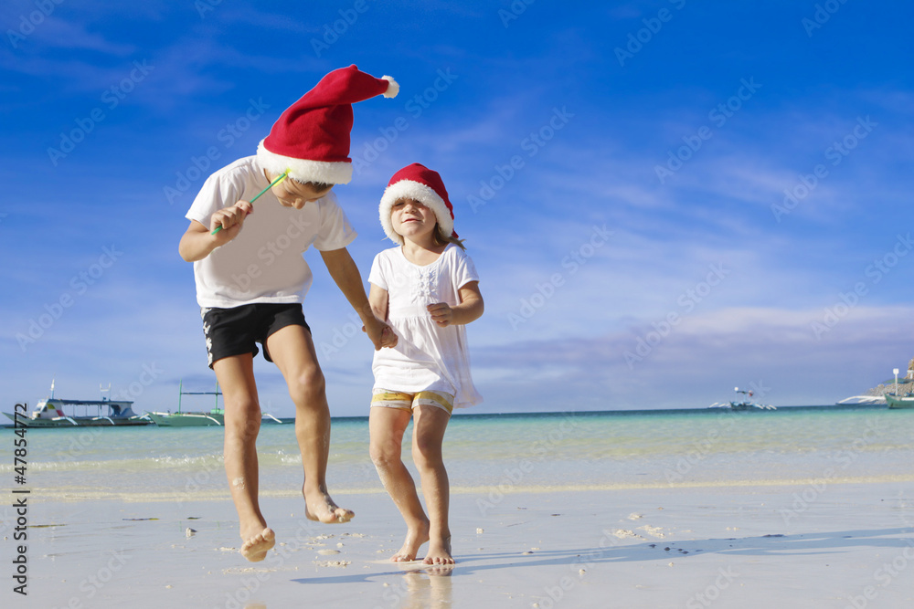 two young happy children in santa hats on tropical beach backgro