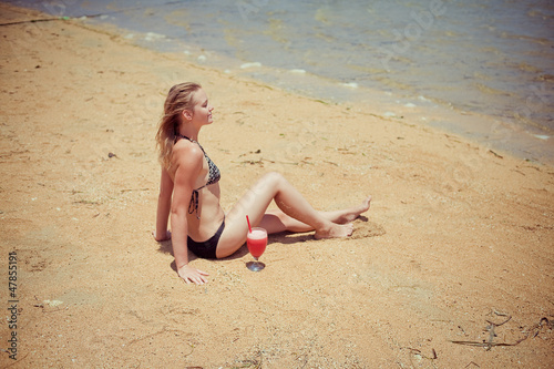 relaxing woman sitting on sand with cocktail 