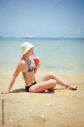 relaxing woman sitting on sand with cocktail 