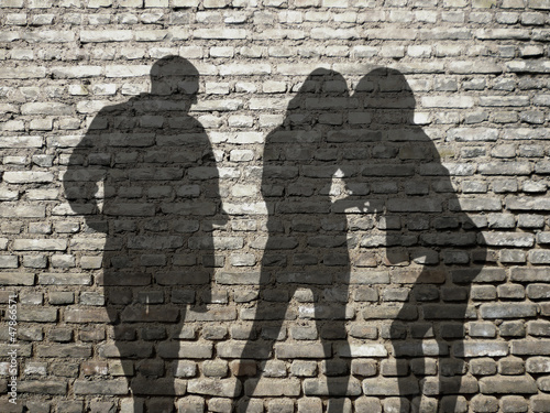 ombres 1 homme 2 femmes sur mur de briques