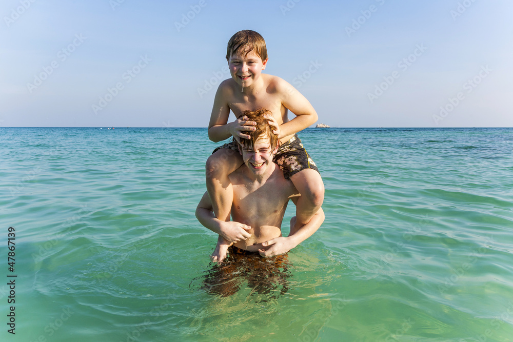 brothers enjoy the  warm water in the ocean and play piggyback
