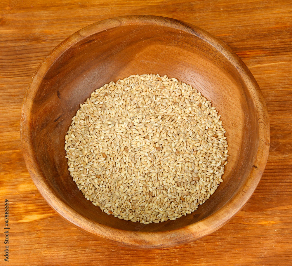 Raw buckwheat in wooden bowl on table on brown background Raw buckwheat in wooden bowl on table on brown background