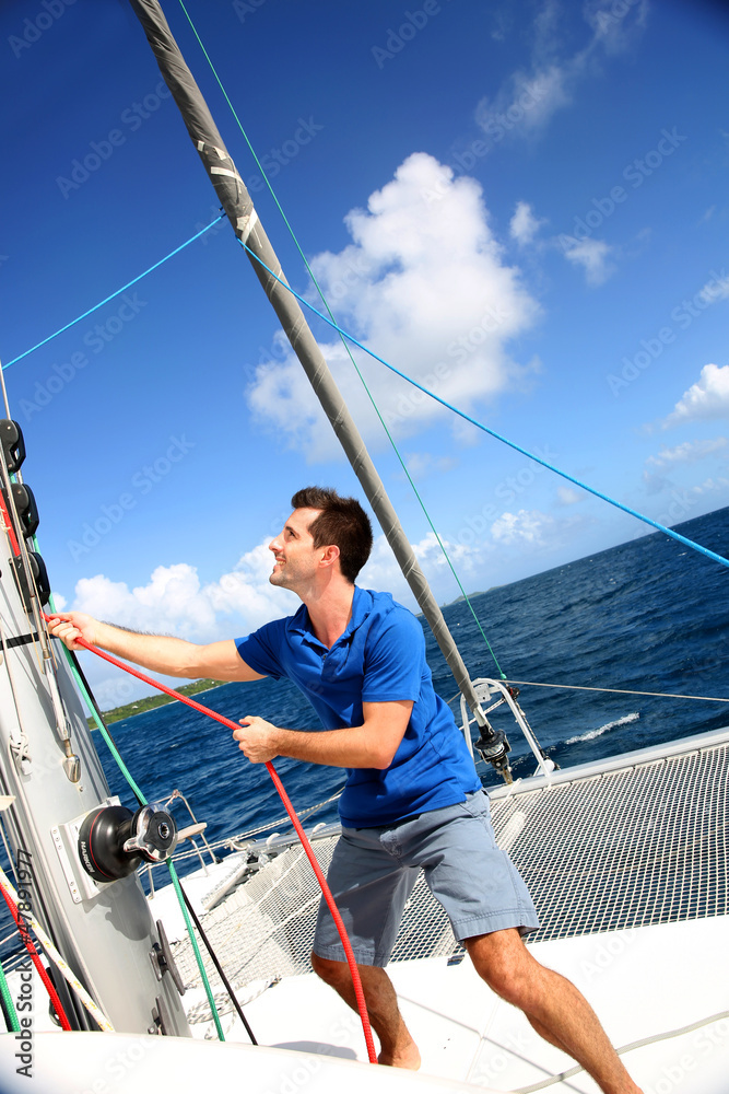 Young man lifting the sail of catamaran during cruising Young man lifting the sail of catamaran during cruising