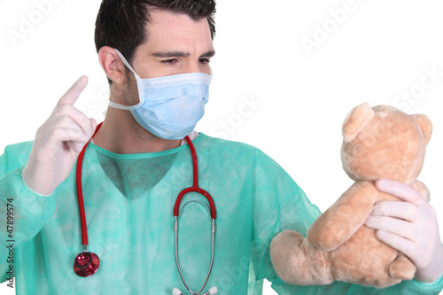 Obraz na plátně Man dressed as a surgeon quarrelling with teddy bear