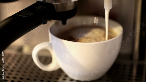 Foamy milk flows into a big white cup of cappuccino