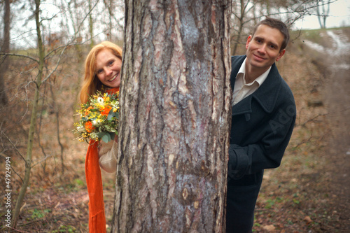 Portrait of a couple smiling and peeping from behind a tree