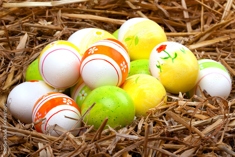 Obraz premium bemalte bunte Eier für Ostern versteckt im Nest aus Stroh