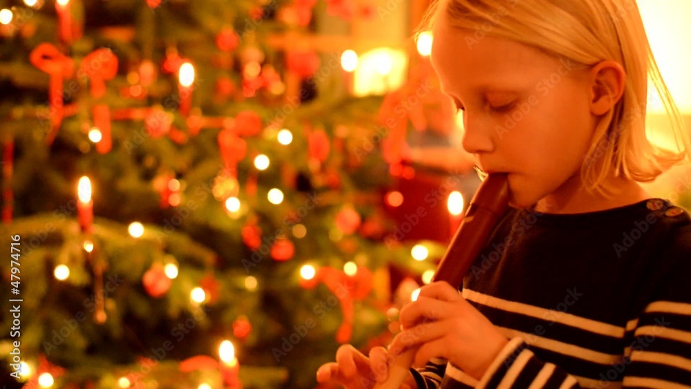 Kleines Mädchen spielt Blockflöte vor Christbaum
