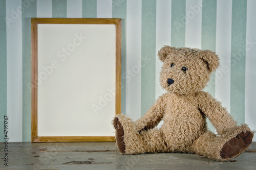 Old teddy bear next to an empty frame