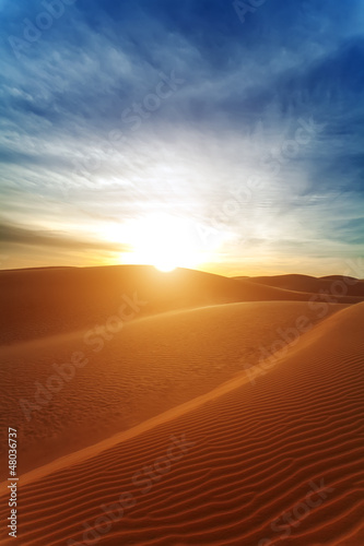 Sandy barkhans in the evening. The sun with beams in the desert.