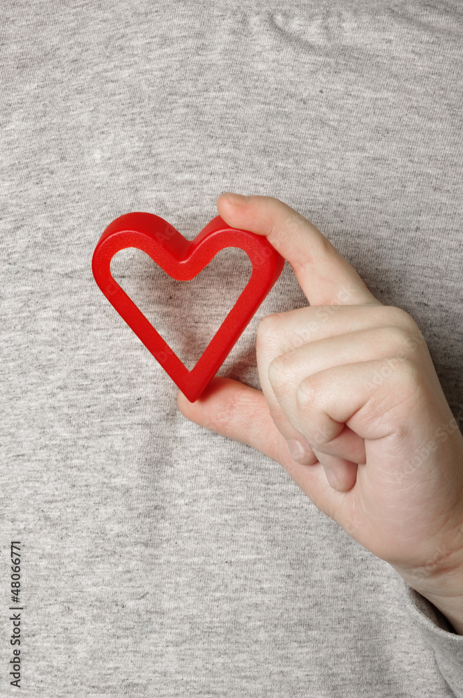 Child's hand with a red heart in the grey background