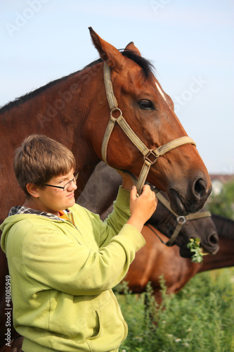 Smiling teenager boy with horses at the field