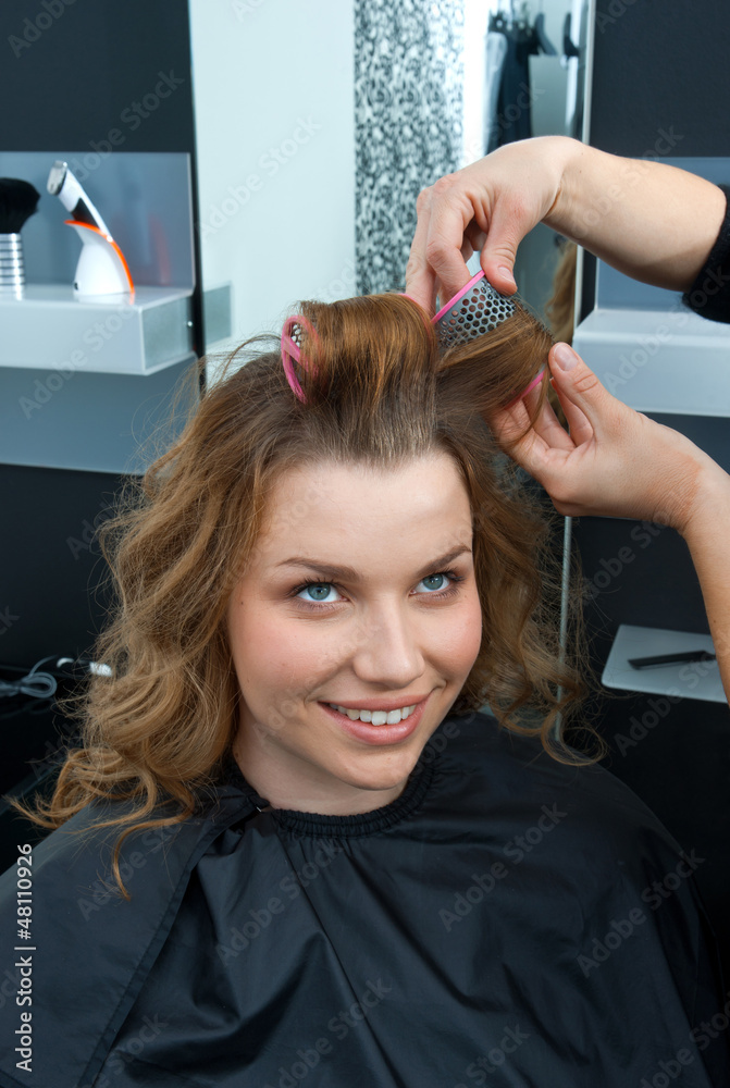 Naklejka premium hair stylist curling woman hair in salon