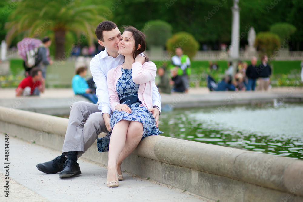 Positive couple sitting by the water in Luxembourg garden of Par