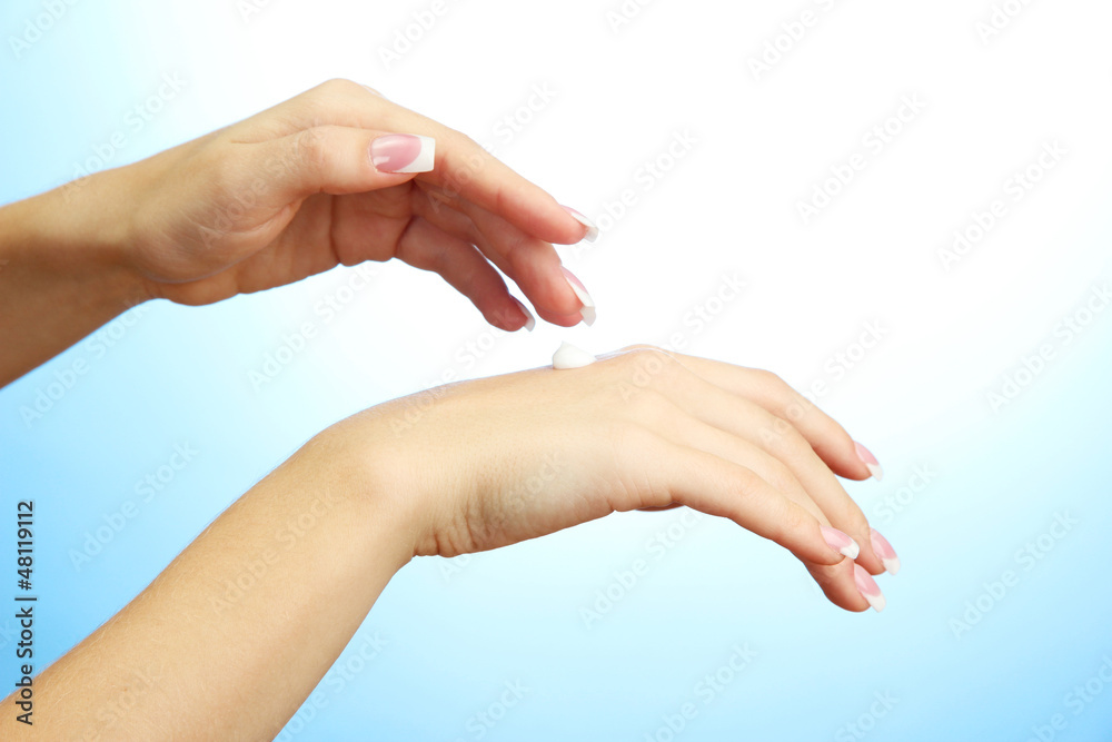 Beautiful woman hands with cream, on blue background