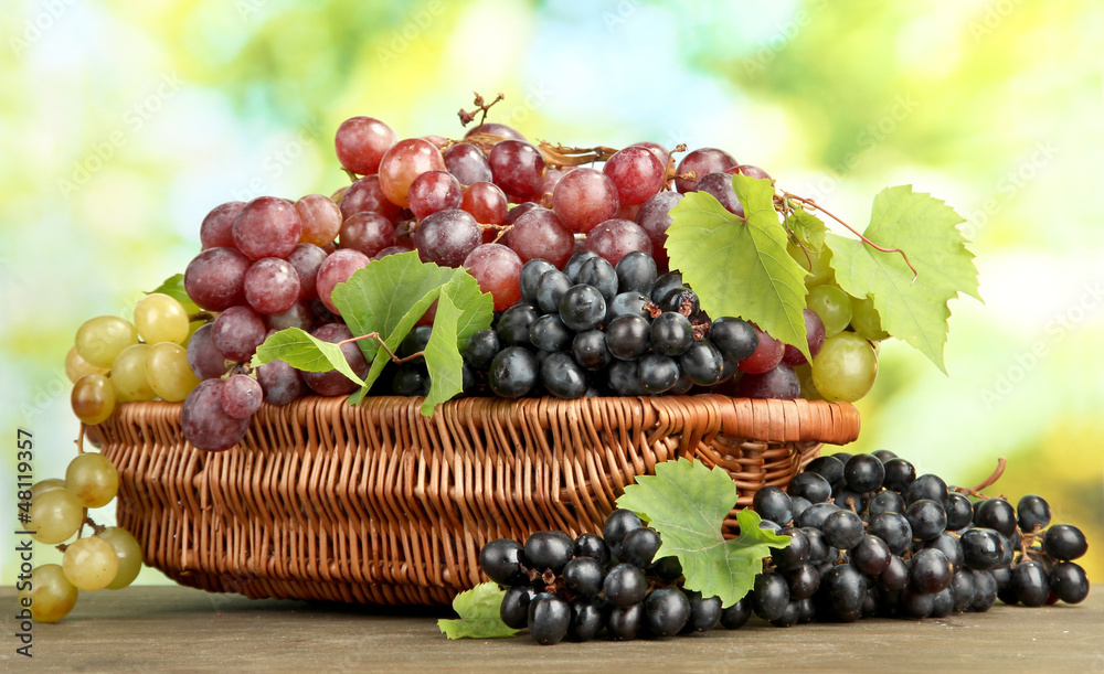 assortment of ripe sweet grapes in basket, on green background assortment of ripe sweet grapes in basket, on green background