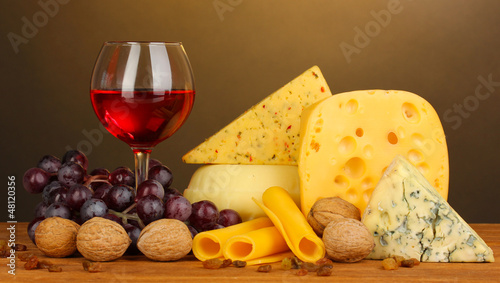 Various types of cheese on wooden table on brown background
