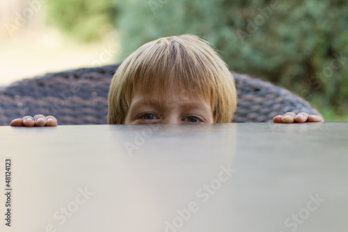 Little boy hiding behind the table photo