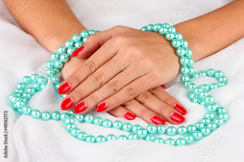 Female hands holding beads on color background