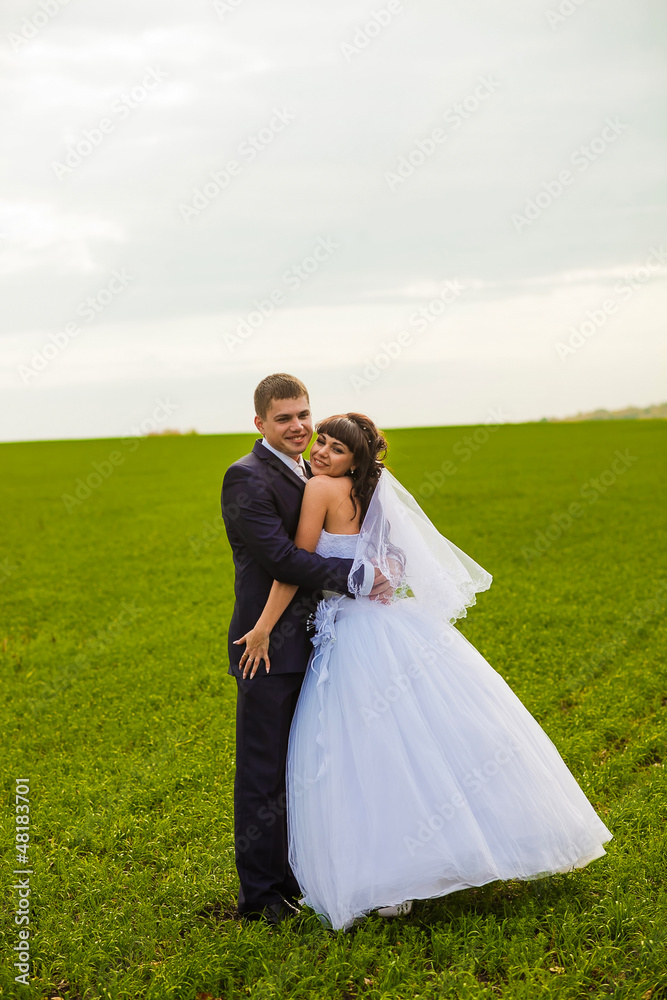 bride and groom outdoor standing in a green field hug, newlyweds